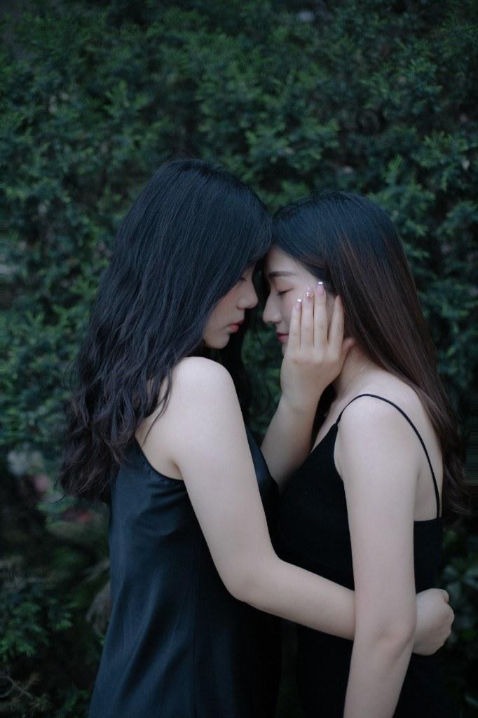 两位闺蜜额头相贴、安静相依,绿叶背景前的亲密陪伴